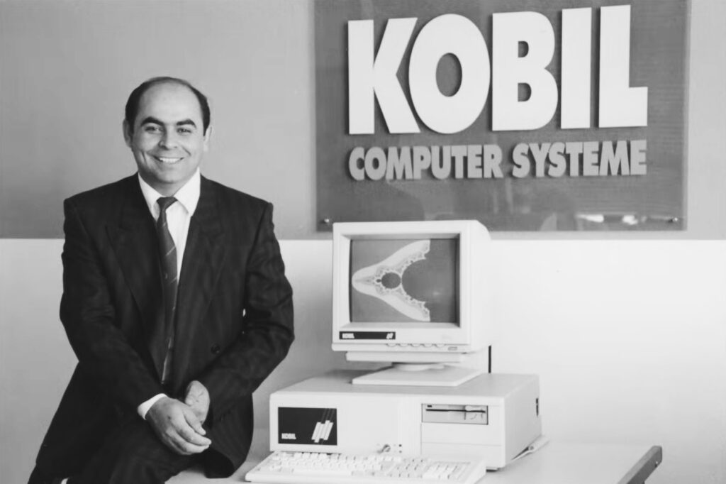 KOBIL-Gründer Ismet Koyun neben einem frühen PC vor einem Schild von KOBIL Computer Systeme